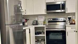 Ett modernt kök med vitvaror i rostfritt stål, inklusive ett kylskåp, en mikrovågsugn och en ugn. På köksbänken står en brödrost, och det finns en skylt som instruerar att fläkten ska sättas på innan ugnen används.