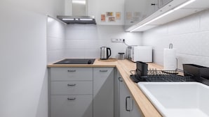 Une cuisine moderne avec des meubles gris, une plaque de cuisson à induction noire, une bouilloire, une machine à café et un évier noir avec un égouttoir en métal.