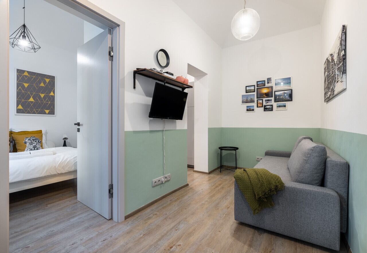 A modern room with a bed, a grey sofa, a TV mounted on a wall, and a small table.