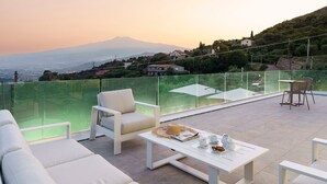 Eine Terrasse mit weißer Möbel, einer Glasbrüstung und Blick auf eine Berglandschaft.