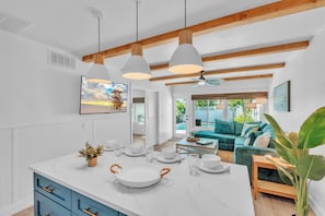 Una cocina moderna con una isla central, luces colgantes y vistas a una zona de piscina.