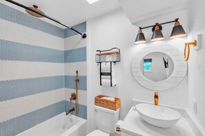 Ein modernes Badezimmer mit Badewanne, Toilette und Waschbecken, mit einer blauen und weißen Mosaikwand, einem runden Spiegel und Handtuchhaltern an der Wand.