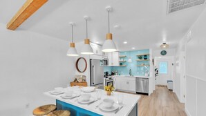 Uma cozinha moderna com armários brancos, uma ilha central com banquetas, iluminação pendente e um painel de azulejos azul.