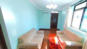 A room with two sofas, a small red table, a ceiling light, and a window with curtains. - New Coffee Tree Hotel (Bukoba)