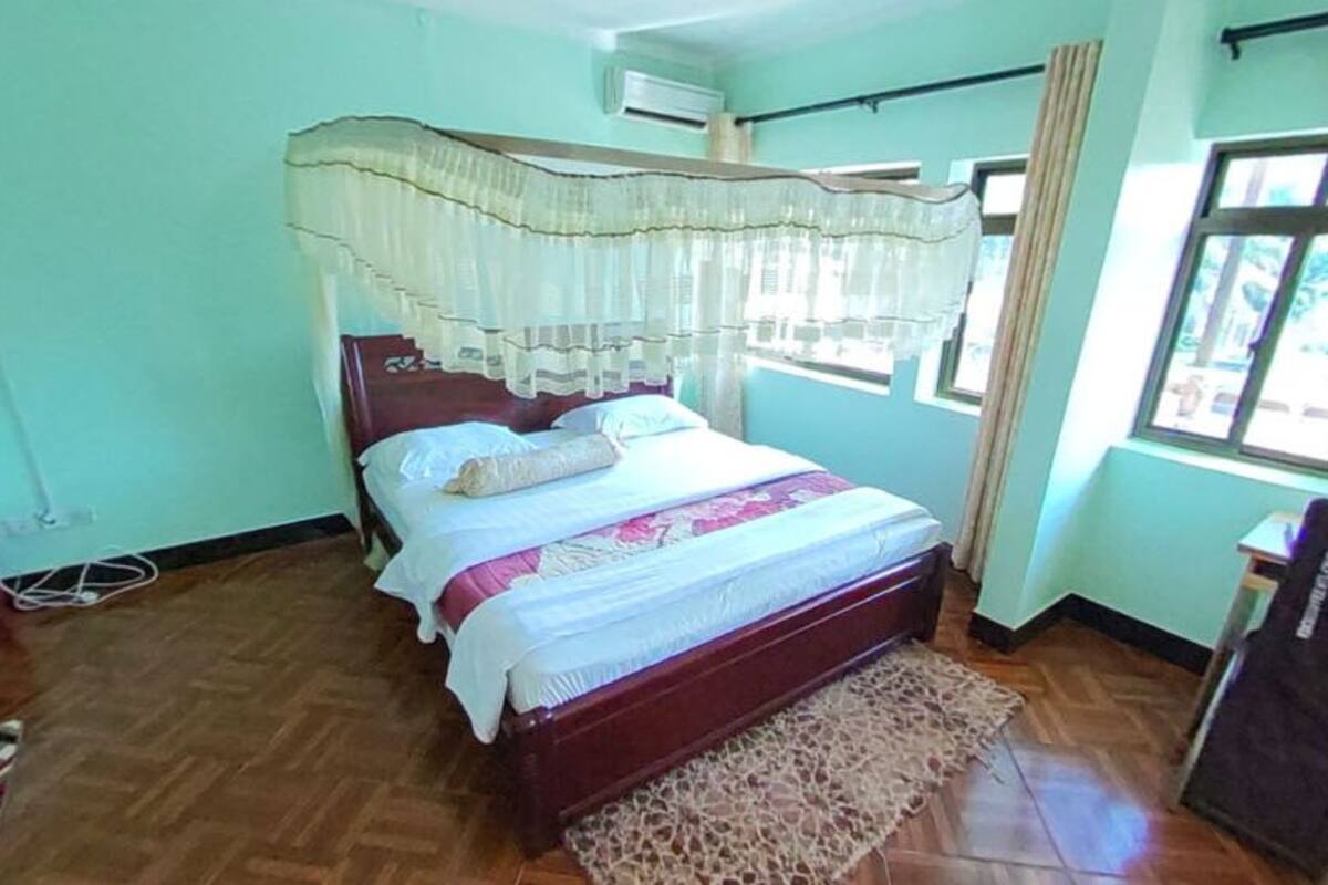 A bedroom with a bed, a small table, a chair, and a window with curtains.