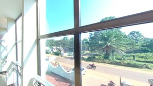 A room with large windows offering a view of a road with vehicles and greenery outside. - New Coffee Tree Hotel (Bukoba)