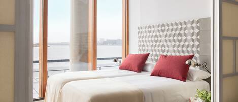 A hotel room with two beds, a view of the water, and a geometric patterned headboard.