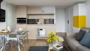 Una cucina moderna con elettrodomestici integrati, una zona pranzo con sedie trasparenti e un soggiorno con divano e tavolino.