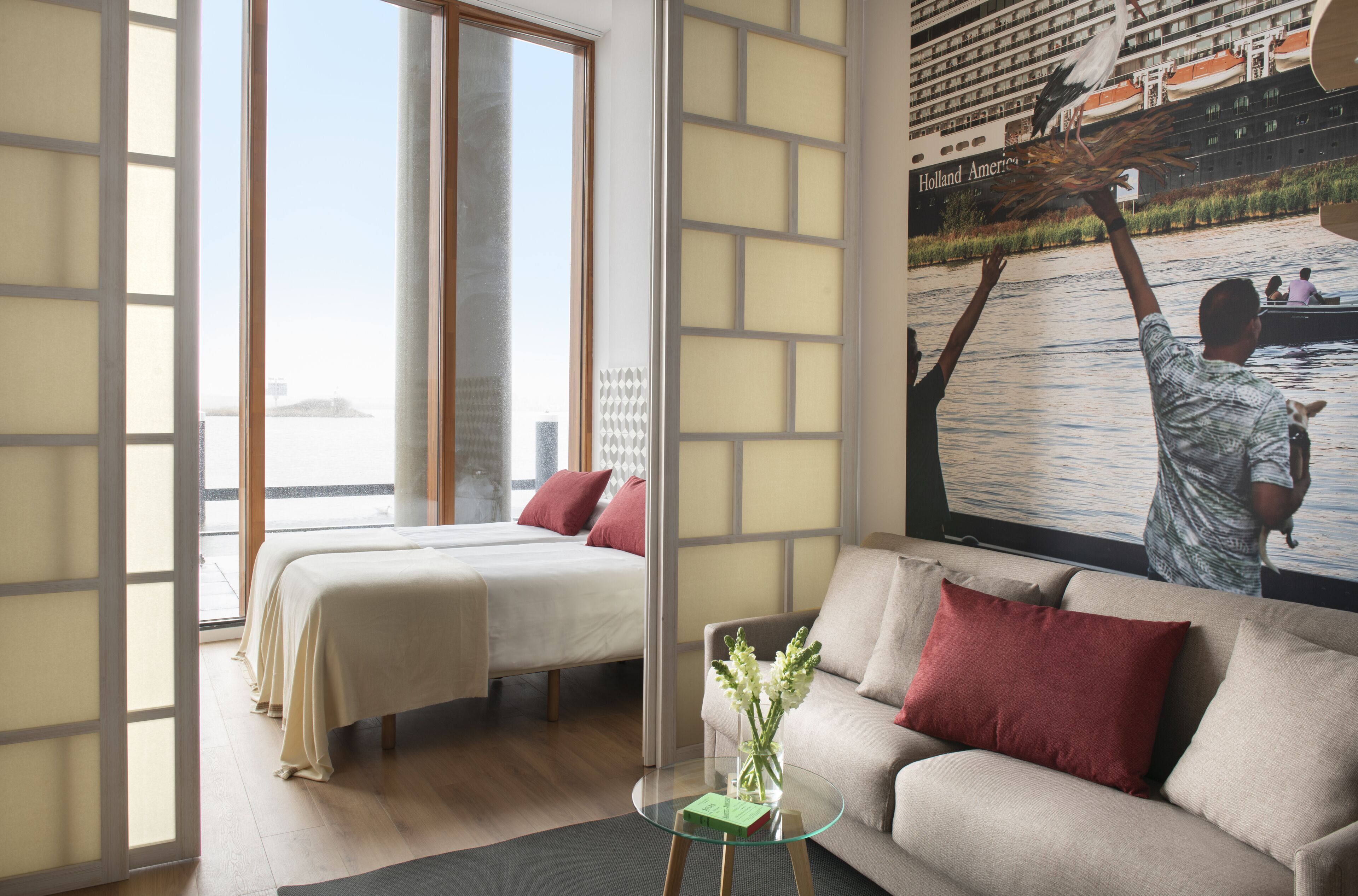 Habitación de hotel con dos camas, un sofá, una mesita de centro de vidrio y un ventanal grande.