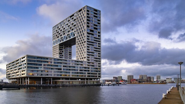 Ein modernes Hochhaus-Hotel mit einem einzigartigen architektonischen Design, das durch einen markanten, übereck hervorstehenden Teil und zahlreiche Balkone gekennzeichnet ist.