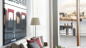 Ein modernes Wohnzimmer mit einer Couch, einem Glastisch und Blick auf eine Stadtlandschaft durch große Fenster.