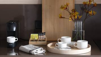 Une table de petit-déjeuner joliment dressée, avec une machine à café, des tasses, un plateau et un vase rempli de fleurs.
