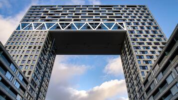 A high-rise building with a prominent geometric structure at the top, multiple floors, and a clear sky with clouds.