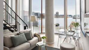 Ein modernes Wohnzimmer mit einer Couch, einem Glastisch und Blick auf einen Fluss und Gebäude.