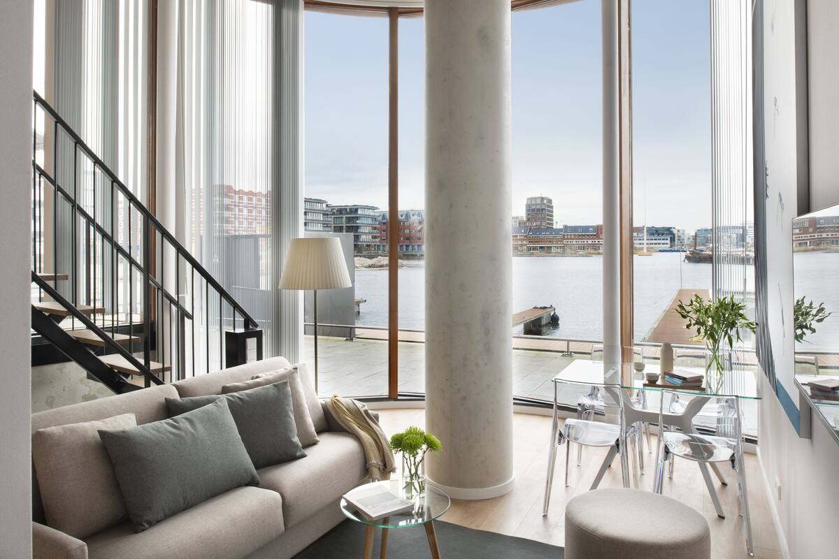 Ein modernes Wohnzimmer mit einer Couch, einem Glastisch und Blick auf einen Fluss und Gebäude.