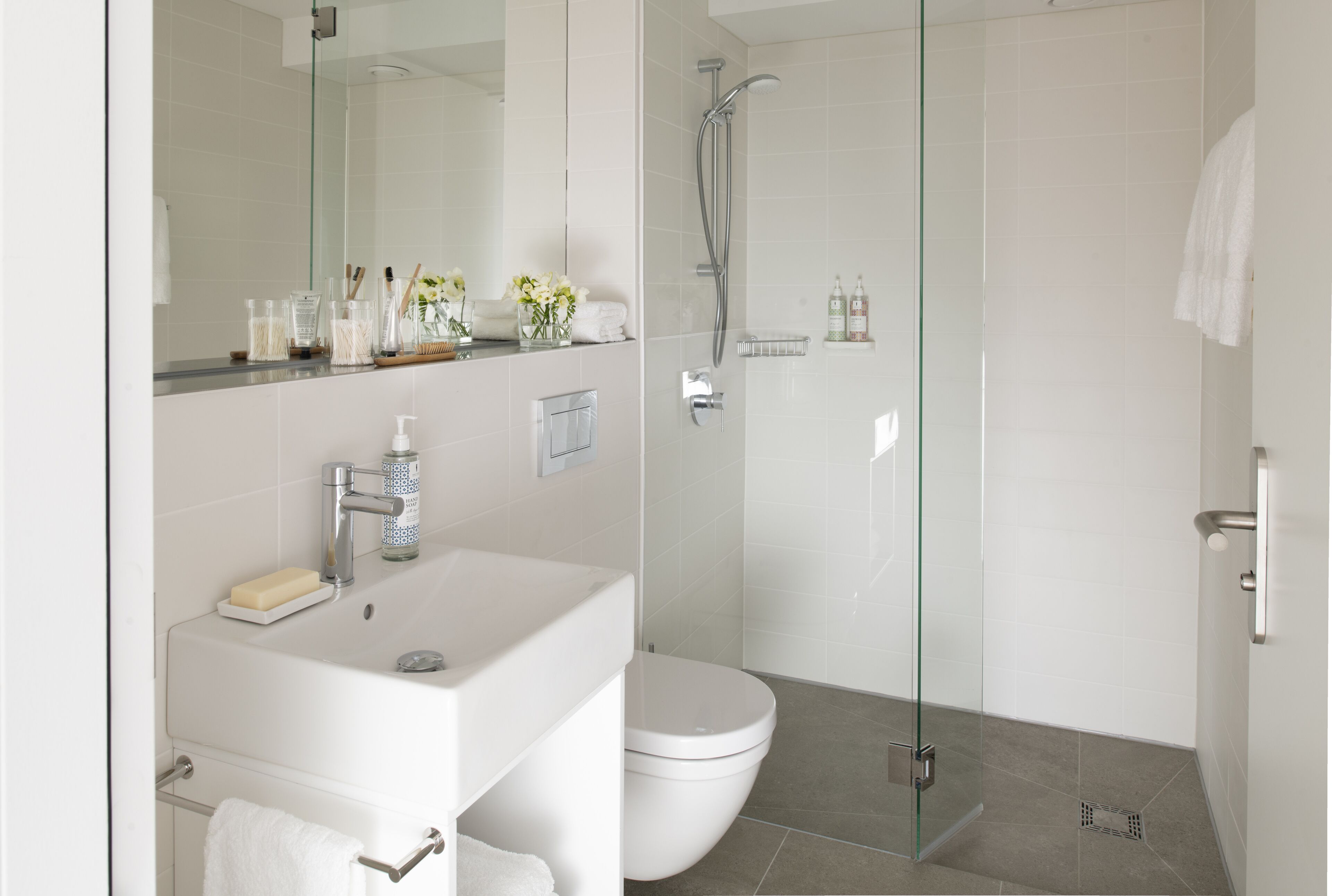 Een moderne badkamer met een glazen douchecabine, een wit wastafelmeubel en een toilet.