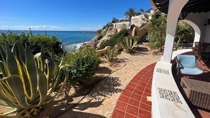 Una propiedad costera con un patio que da al mar, con un sendero de piedra, una gran planta de agave y mobiliario de exterior.