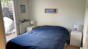 A bedroom with a large bed, a bedside table with a lamp, a radiator, and a window with a view of the outdoors. - Maison AU Calme, Quiet House, 20 Minutes Bordeaux (Gradignan)