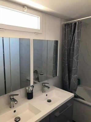Ein Badezimmer mit zwei Waschbecken, einem großen Spiegel und einer Duschvorhang.