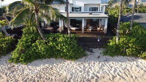 A beachfront property with a covered patio, palm trees, and a sandy beach.