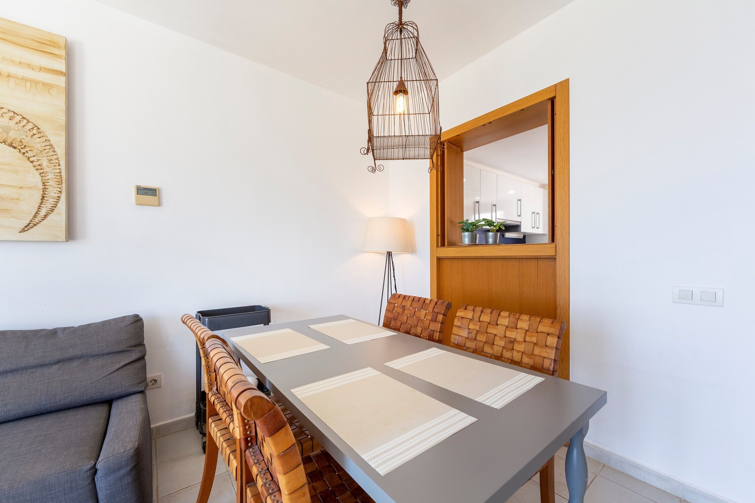 Een eetruimte met een lange tafel, comfortabele stoelen, een hanglamp en een kunstwerk aan de muur.