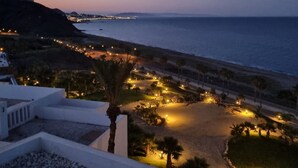 Un complex turístic a la costa amb vistes al mar, una platja ben il·luminada i una palmera.