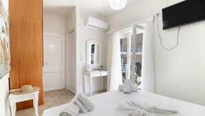 A hotel room with a bed, a desk, a mirror, an air conditioning unit, a television, and a balcony with a view. - M1 Room with Wi-Fi and Air Conditioning (Lefkada)