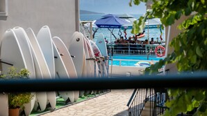A poolside area with surfboards, a boat, and a mountainous backdrop. - M1 Room with Wi-Fi and Air Conditioning (Lefkada)