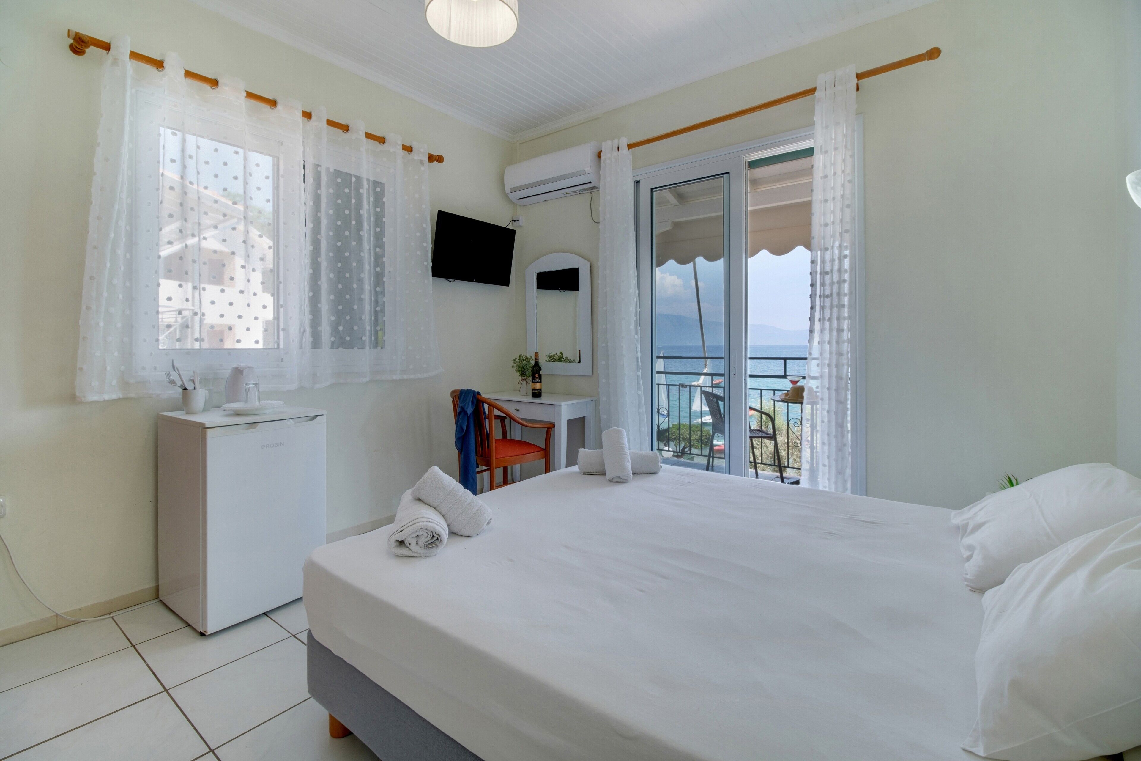 A hotel room with a bed, a desk, a chair, a TV, and a balcony with a view.