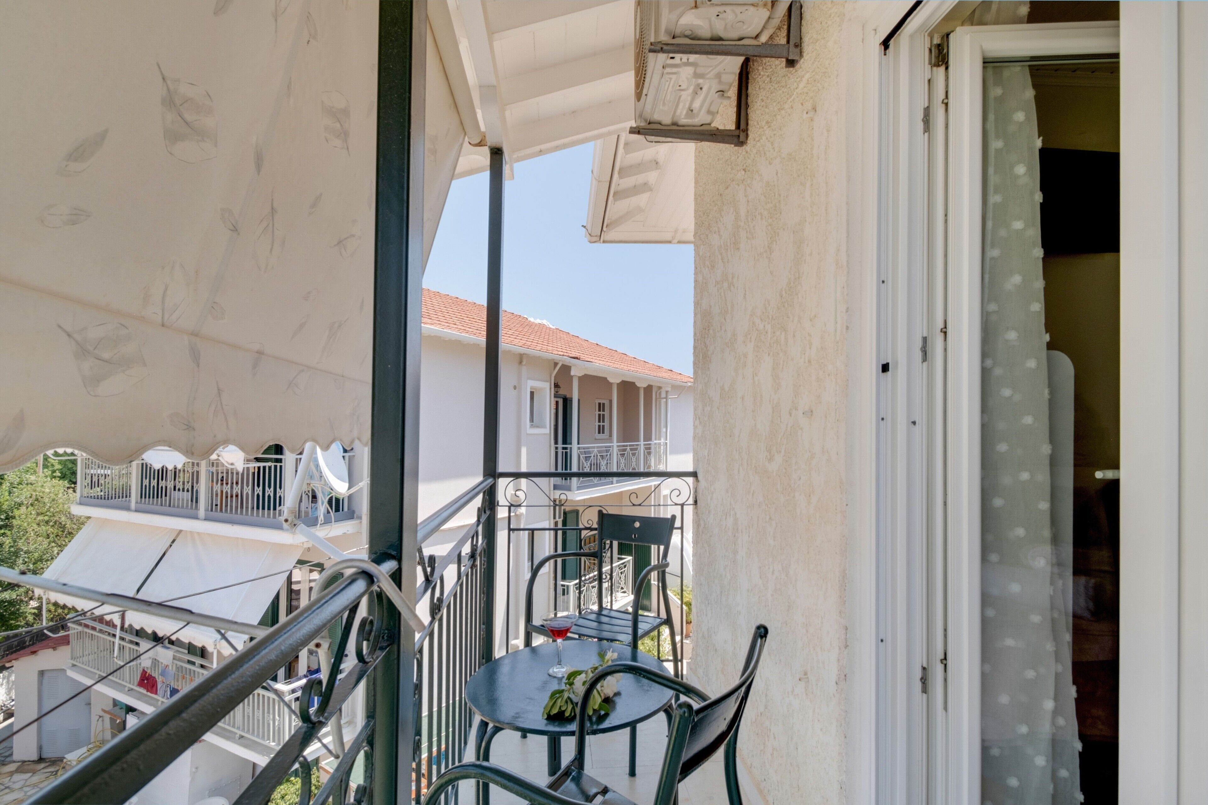 Uma varanda com mesa e cadeiras, vista de um edifício com telhado vermelho e uma porta com cortina.