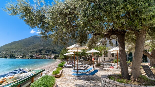 A stone-paved beach area with lounge chairs and umbrellas, a row of boats, and a view of the sea and hills. - 'M3 Room' with Wi-Fi and Air Conditioning (Lefkada)