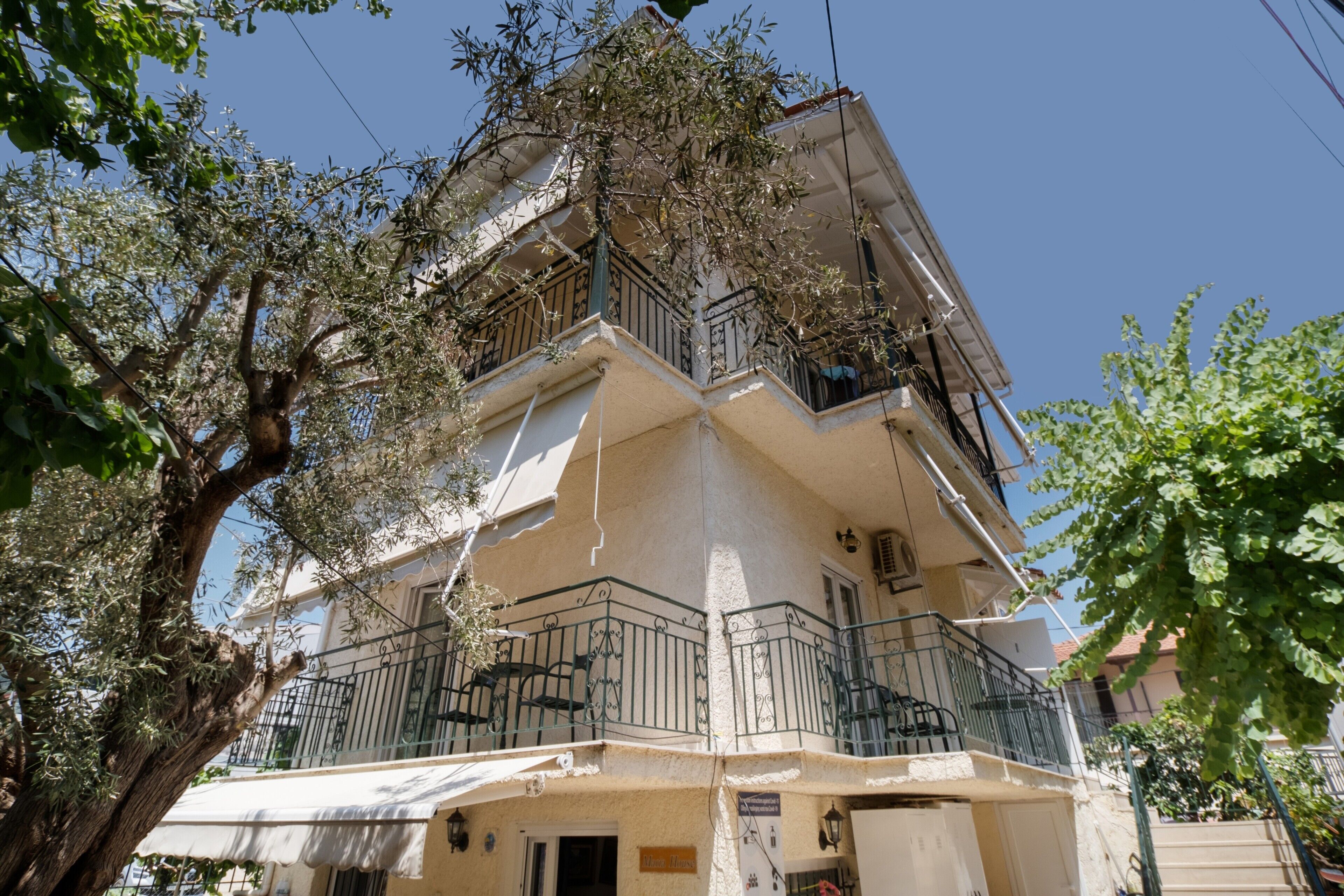 A multi-story building with balconies, a tree in the foreground, and a clear sky.