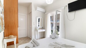 Een hotelkamer met een bed, bureau, spiegel, airconditioning, televisie en een balkon met uitzicht.
