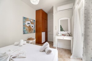 A hotel room with a bed, a wooden wardrobe, a desk with a mirror, a painting on the wall, and a window with sheer curtains. - M4 Room with Wi-Fi and Air Conditioning (Lefkada)