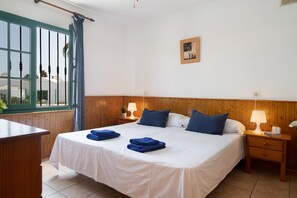 A neatly made bed with blue towels, wooden headboard, bedside lamps, and a window with curtains.