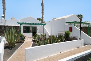 A white building with a green roof, a door, and a small garden area with plants.