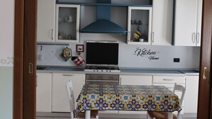 A kitchen with white cabinets, a blue range hood, a tiled backsplash, and a table with a patterned tablecloth.