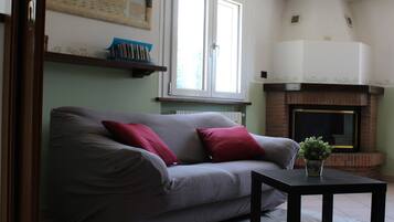 Een woonkamer met een bank, een bijzettafeltje, een open haard en een raam.