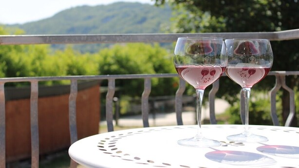 Two wine glasses on a table with a view of greenery and hills in the background.