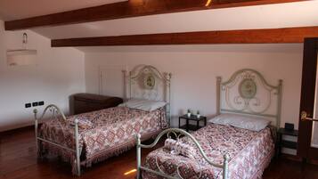 A room with two metal beds, a small bedside table with a plant, a wooden ceiling, and a door.