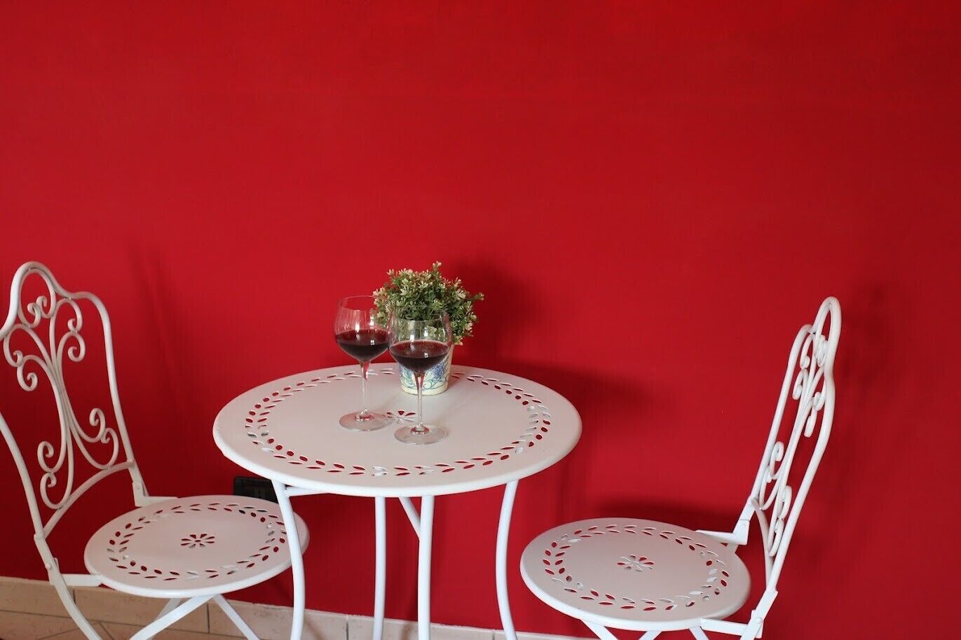 Een set witte metalen tafel en stoelen voor een rode muur.