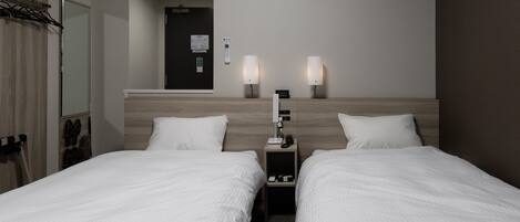 A hotel room with two beds, a bedside table with a lamp, a wall-mounted air conditioner, and a door with a mirror and shoe rack.