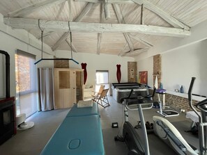 Une pièce spacieuse équipée d’un sauna, d’appareils de musculation, d’une table de massage et d’une cheminée.