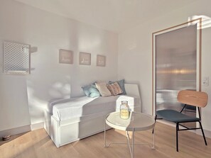 Ein modernes Zimmer mit einem weißen Sofa, einem kleinen runden Tisch mit einer Flasche, einem Sessel und einer Wandleuchte.