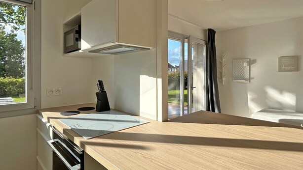 A modern kitchen with a built-in oven, a black knife block, and a window with a view of greenery.