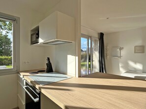 Een moderne keuken met een inbouwoven, een zwart messenblok en een raam met uitzicht op groen.