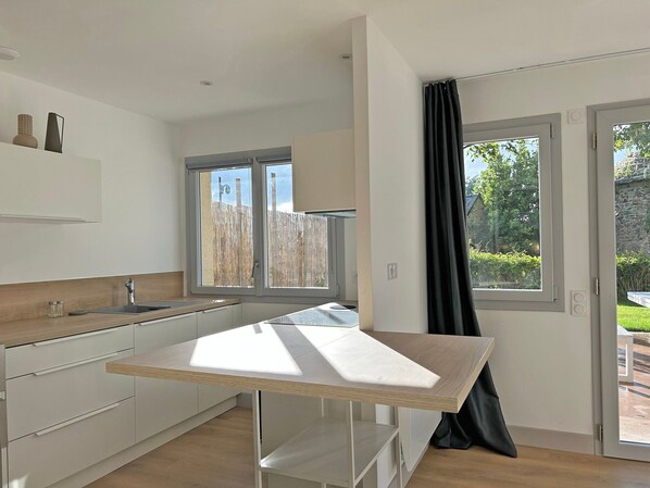 Et moderne køkken med en central ø, et vindue med udsigt, og en dør der fører til en balkon.