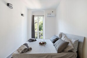 A neatly made bed with pillows and a tray of items, a window with curtains, and a wall-mounted air conditioner.