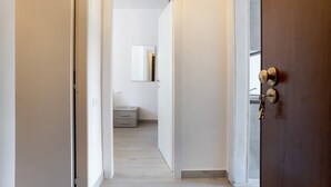 Un couloir avec une porte en bois sur la droite, un miroir accroché au mur et un petit meuble à tiroirs au fond.