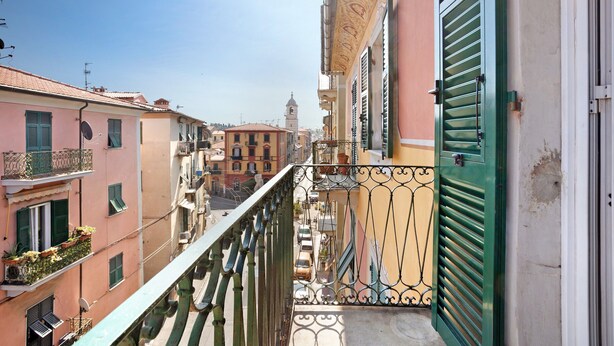 Un balcon offrant une vue sur les bâtiments voisins, un ciel dégagé et une tour lointaine.